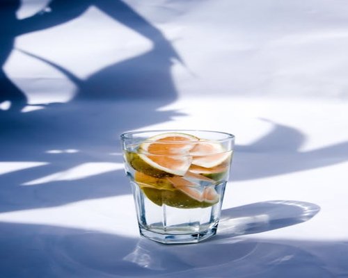 A tall transparent glass filled with cold water next to fresh citrus slices under bright summer daylight