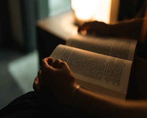 A person enjoying a quiet evening reading a book under a warm personal reading light at home